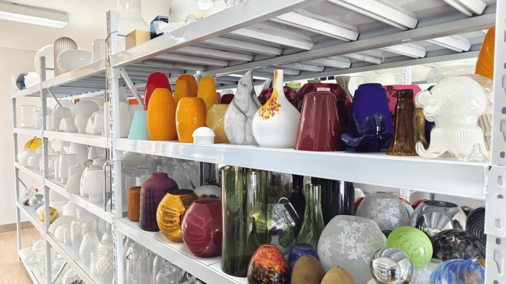 Variety of colorful glass lampshades and ceramic vases in a manufacturing warehouse.