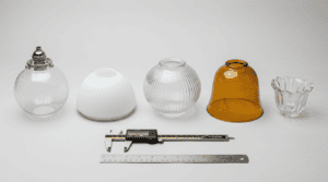 Glass lamp shade replacement options arranged with caliper and ruler: clear seeded, frosted opal, ribbed schoolhouse, amber cased, chandelier cup