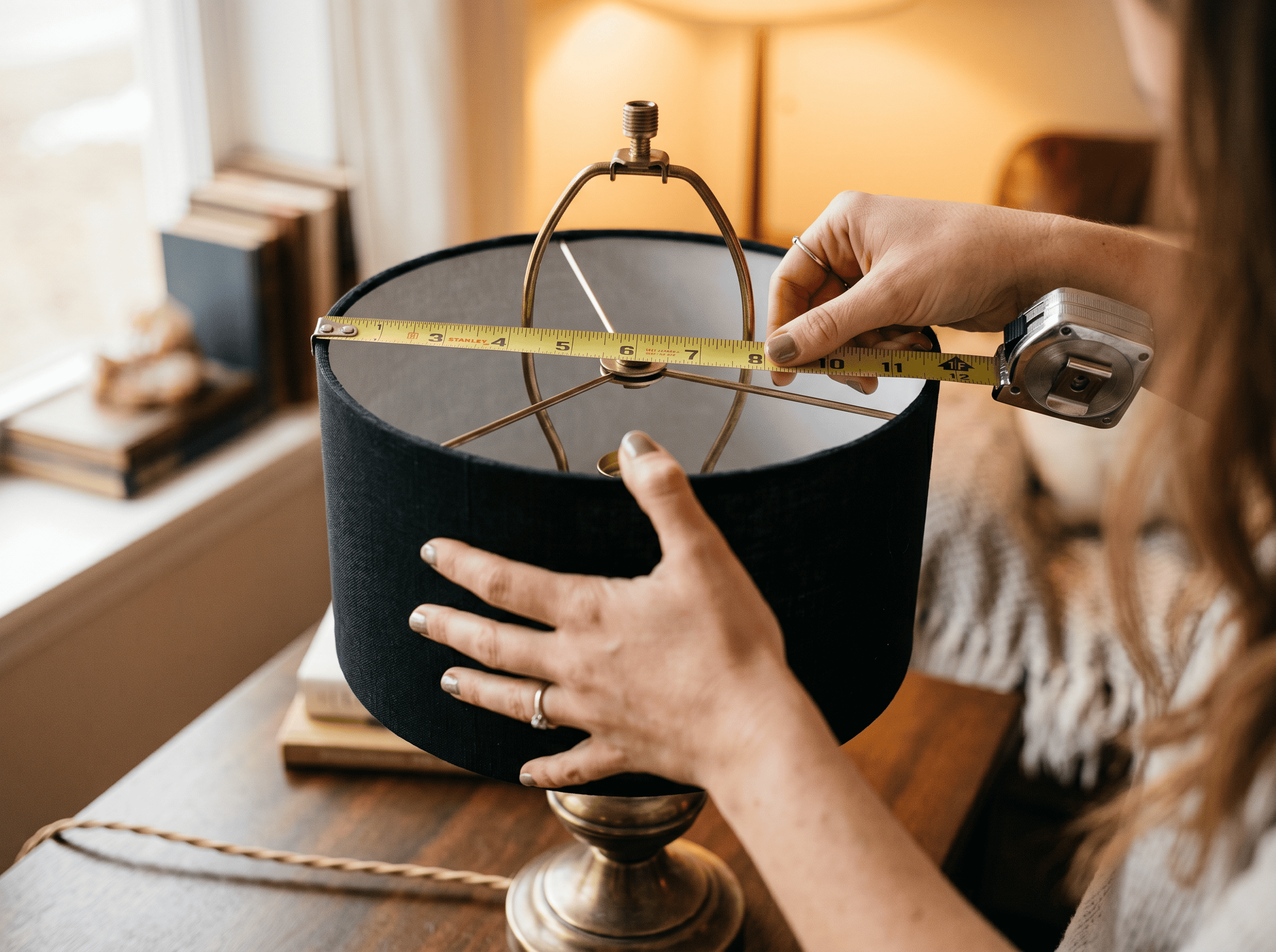 Person measuring a glass lampshade for custom lighting design.