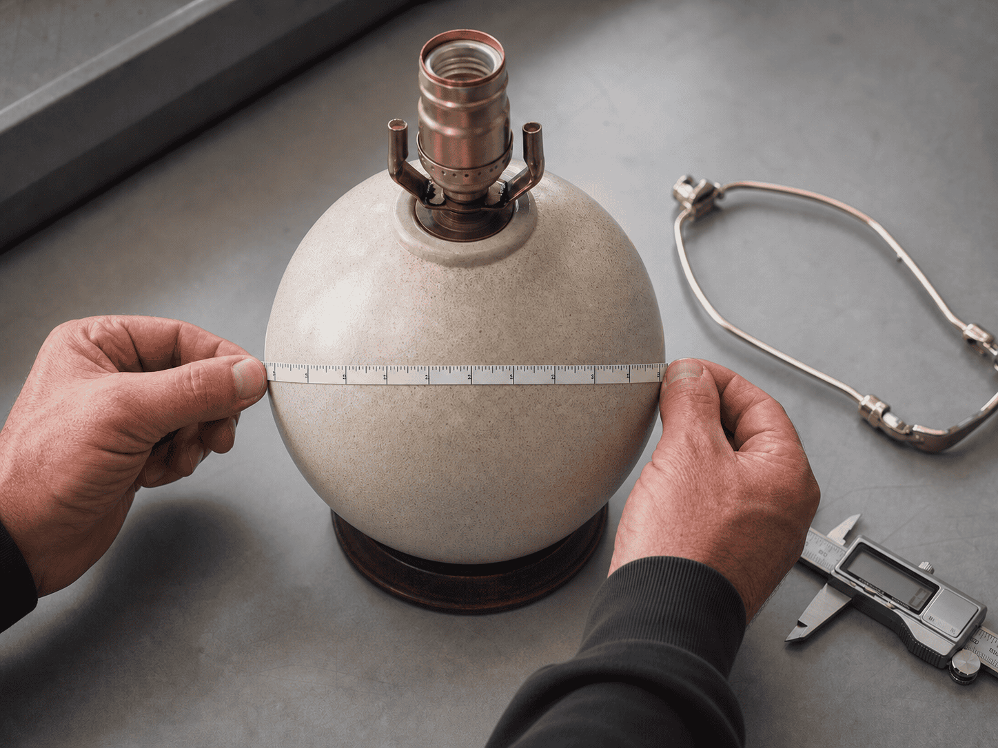Person measuring a glass lampshade with a tape measure for quality control.