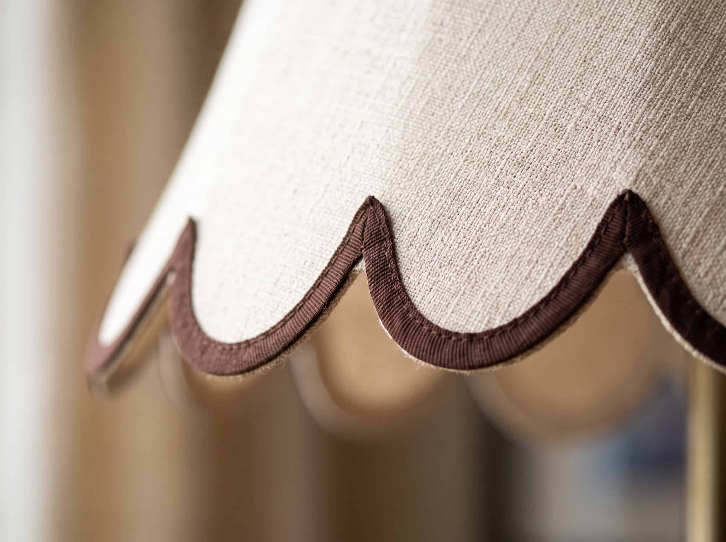 Nahaufnahme eines beigefarbenen Stofflampenschirms mit braunem Kantenabschluss.