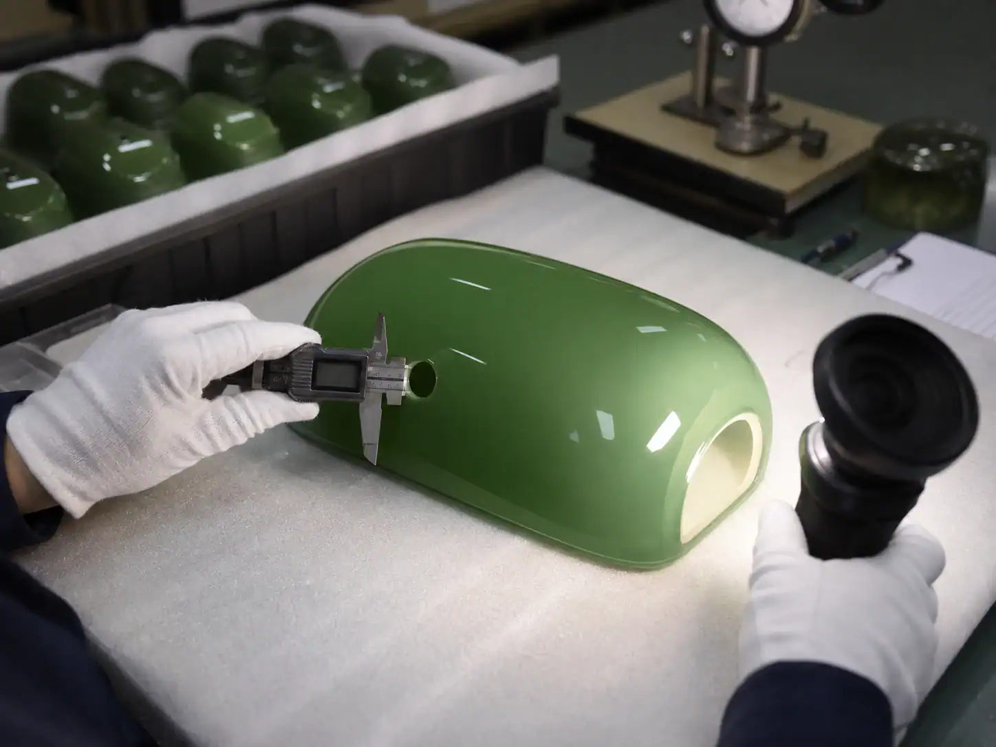 Green glass lampshade being inspected in a factory setting.