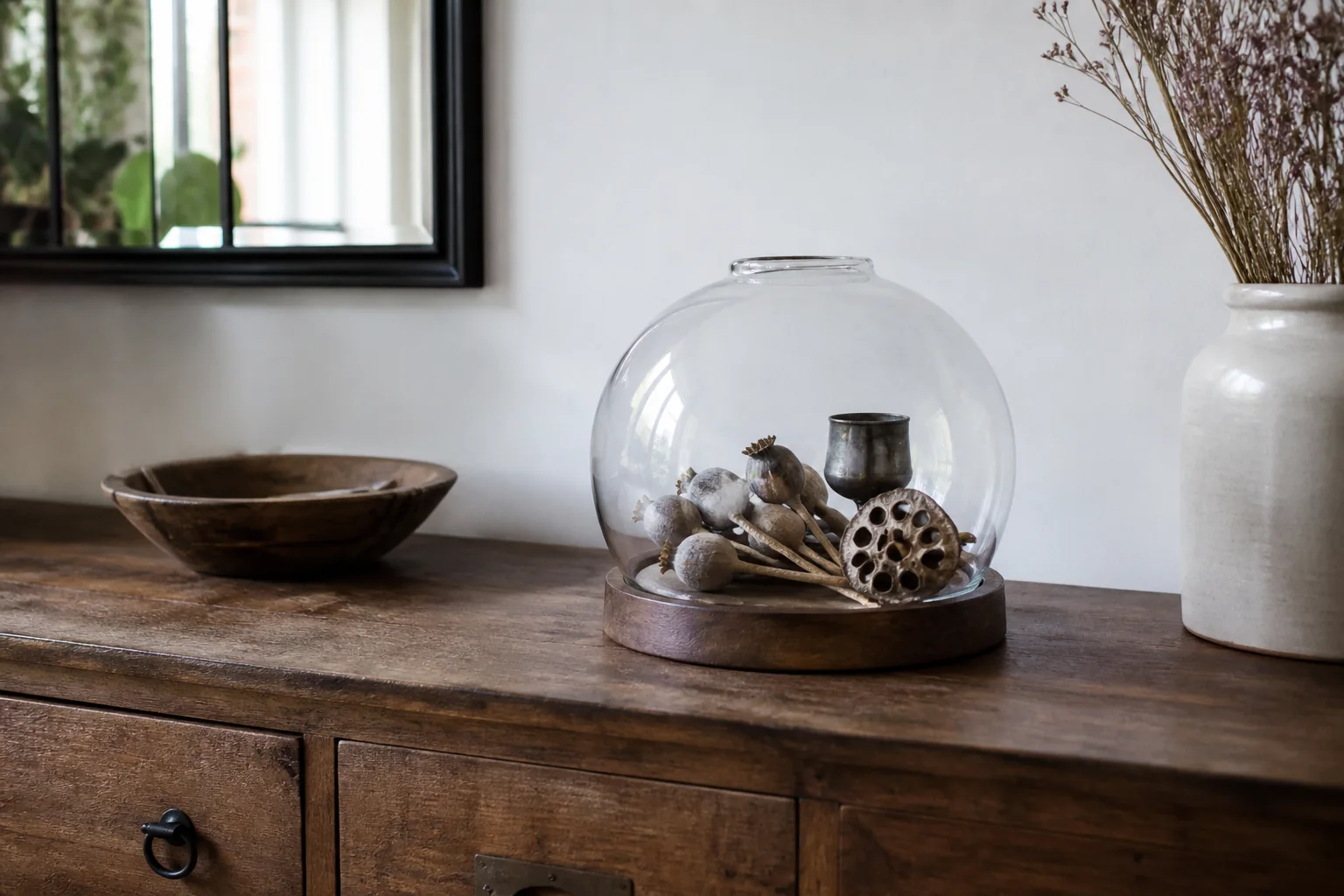 Un abat-jour en verre vintage clair posé sur une base en bois adaptée et réutilisé comme cloche sur des végétaux séchés