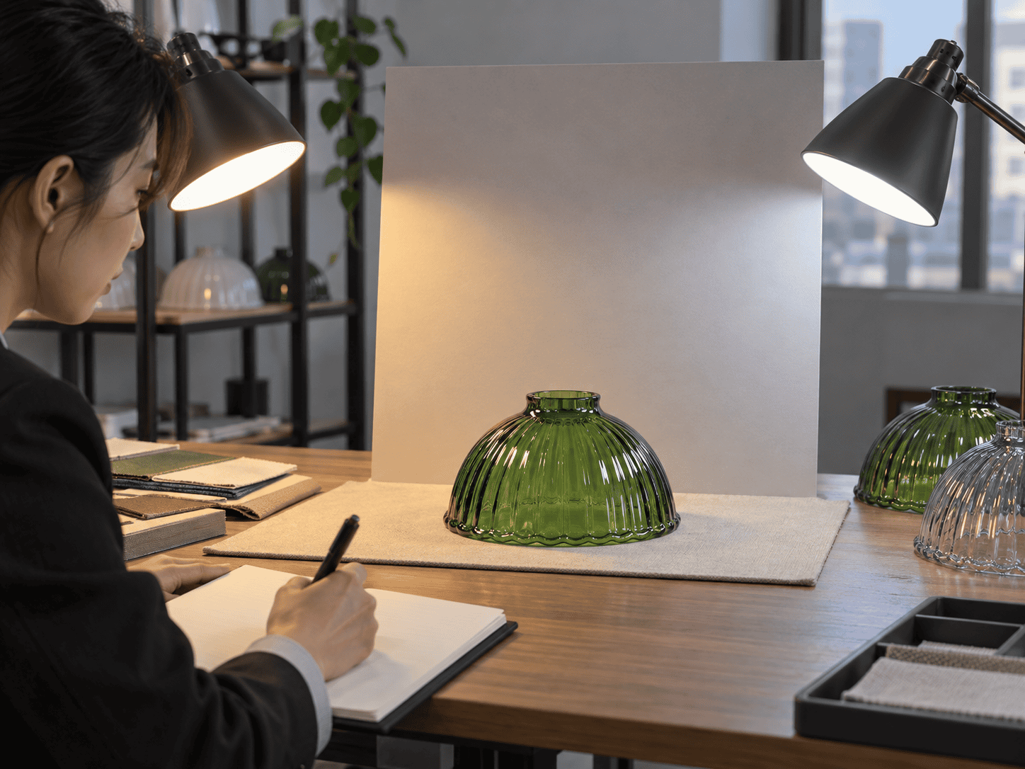 Lighting buyer comparing a green glass lamp shade against an unprinted reference board under warm and neutral controlled lights