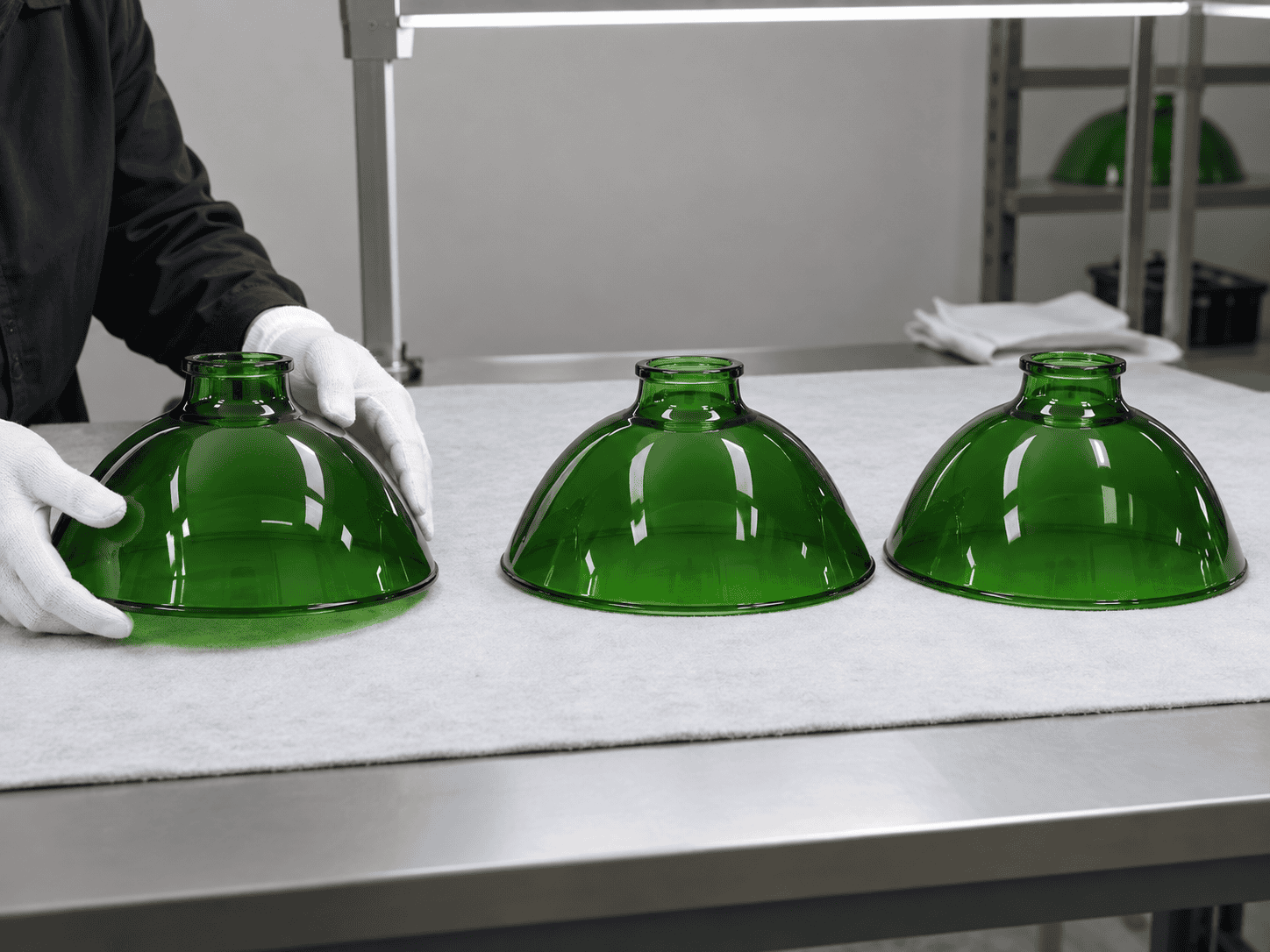 Green glass lampshades being crafted in a factory setting.